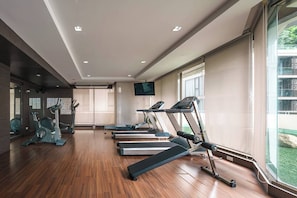 Ein Fitnessraum mit Trainingsgeräten, einem Fernseher und großen Fenstern.