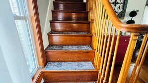 Una escalera de madera con barandilla, alfombras estampadas en cada peldaño y un adorno en la pared.