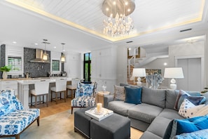 A modern living room with a grey sofa, patterned armchairs, and a dining area with white cabinetry and a black backsplash. - NEW! Ultra Luxe Home, Walk to 5th Ave w/ Spa (Naples)