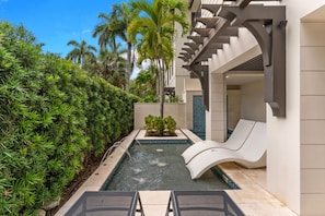 A pool with a slide, surrounded by lush greenery and a modern building with a balcony. - NEW! Ultra Luxe Home, Walk to 5th Ave w/ Spa (Naples)
