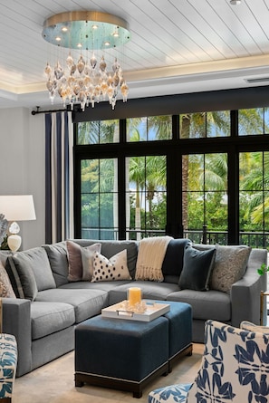 A modern living room with a sectional sofa, ottoman, and chandelier. - NEW! Ultra Luxe Home, Walk to 5th Ave w/ Spa (Naples)