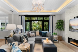 A modern living room with a sectional sofa, a fireplace, and large windows. - NEW! Ultra Luxe Home, Walk to 5th Ave w/ Spa (Naples)