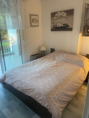 A bedroom with a bed, a nightstand, a lamp, and a window with a view of greenery. - Rent beautiful duplex near Le Lavandou only from 11 to 18 /07 and after 22 08 (le lavandou)
