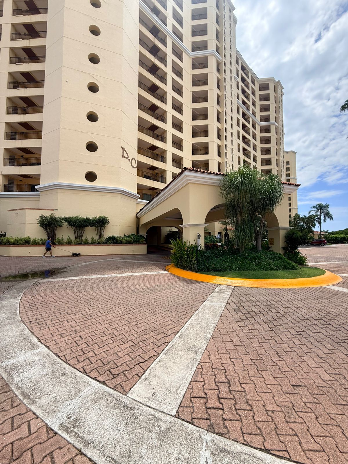 A multi-story hotel with a central courtyard, a covered entrance, and a landscaped area with a palm tree.