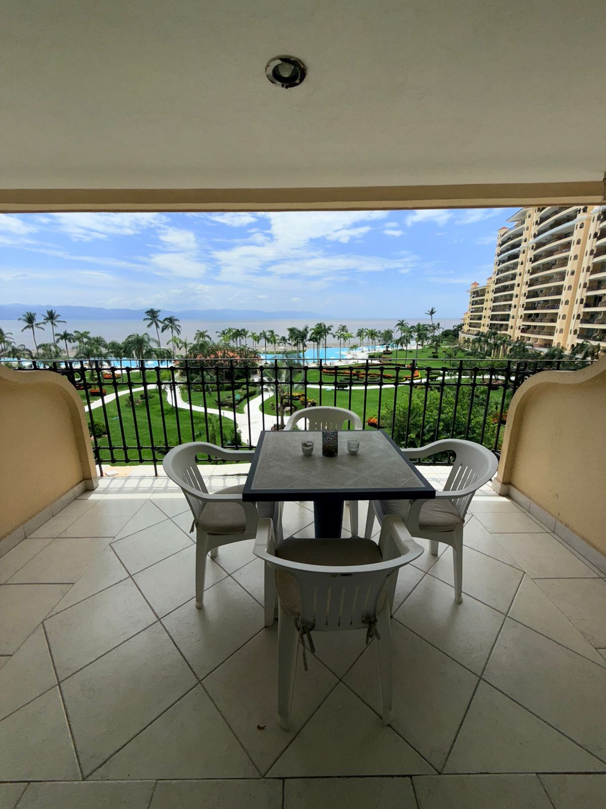 A balcony with a table and chairs, overlooking a pool and palm trees.