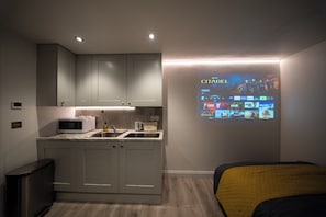 A modern kitchen with a built-in microwave, toaster, and sink, and a projection screen displaying a movie. - Contemporary Studio, London Prime Location (London)