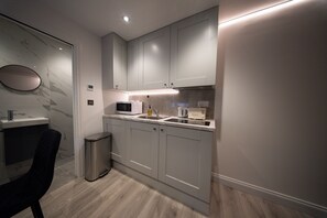 A modern kitchen with grey cabinets, a microwave, a sink, and a trash bin. - Contemporary Studio, London Prime Location (London)