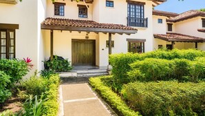 Une maison à deux étages, avec un toit en tuiles, un balcon et un jardin bien entretenu.