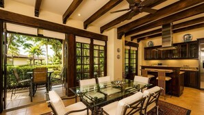 Un coin repas avec une table et des chaises en verre, un ventilateur de plafond et une vue sur un jardin.