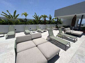 Eine Dachterrasse mit mehreren Liegestühlen und einer Sitzecke, umgeben von einer weißen Mauer und tropischen Pflanzen.