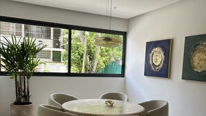 Un espace repas moderne avec une table ronde et six chaises, une plante en pot et deux tableaux abstraits accrochés au mur.