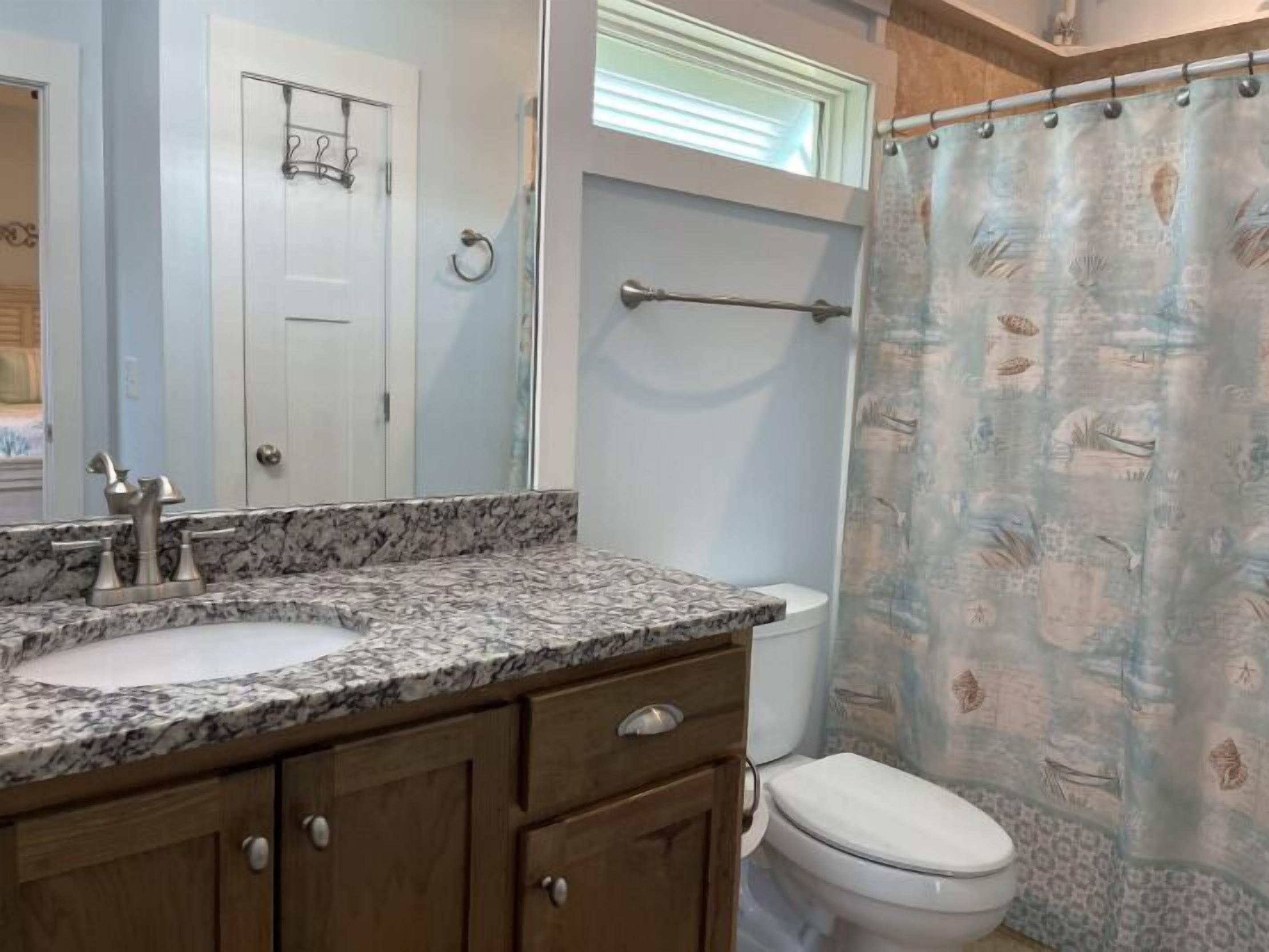 Une salle de bain avec un comptoir en marbre, des meubles en bois, des toilettes et un rideau de douche.