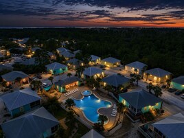 Un resort con varias casas, una piscina y vista al océano al atardecer.