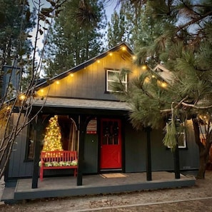 A wooden cabin with a red door, a bench, and a Christmas tree. - THE OHANA at BIG BEAR (Big Bear)