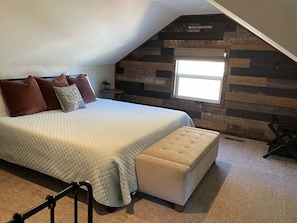 A bedroom with a bed, a window, a wall with a wooden panel design, and a small table with a plant. - THE OHANA at BIG BEAR (Big Bear)