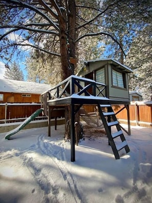 A treehouse with a ladder and slide, surrounded by snow. - THE OHANA at BIG BEAR (Big Bear)