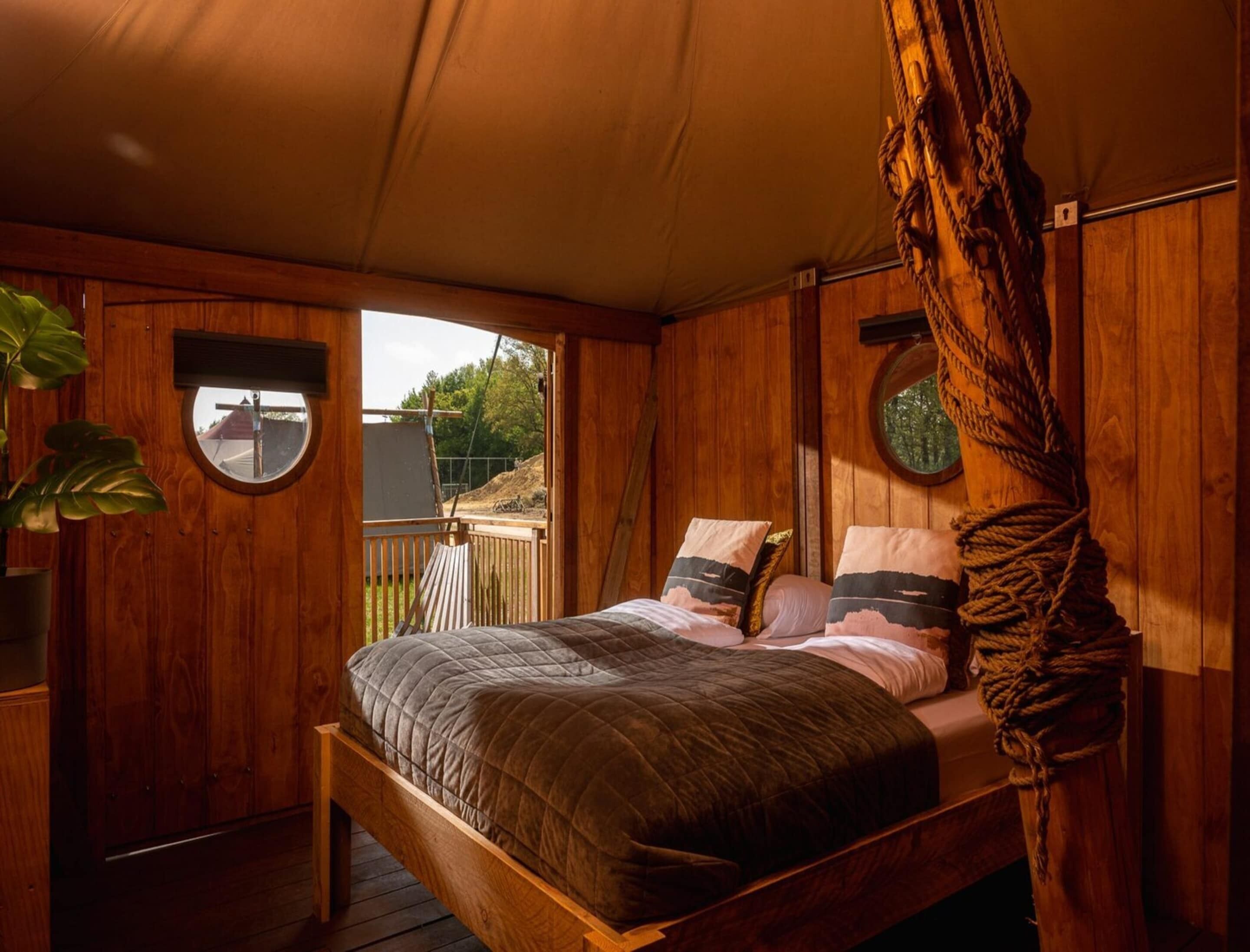Ein Schlafzimmer in einer Holzhütte mit einem Bett, zwei Fenstern und Blick ins Freie.