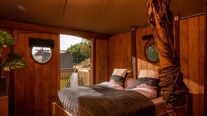 Ein Schlafzimmer in einer Holzhütte mit einem Bett, zwei Fenstern und Blick ins Freie.