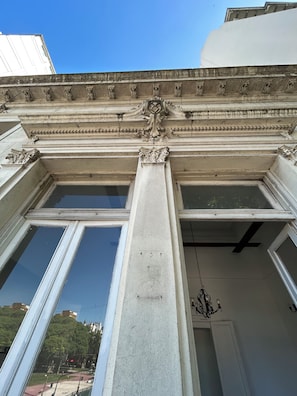 Fachada de edificio con elementos arquitectónicos clásicos, incluyendo una columna central y detalles ornamentales sobre las ventanas.