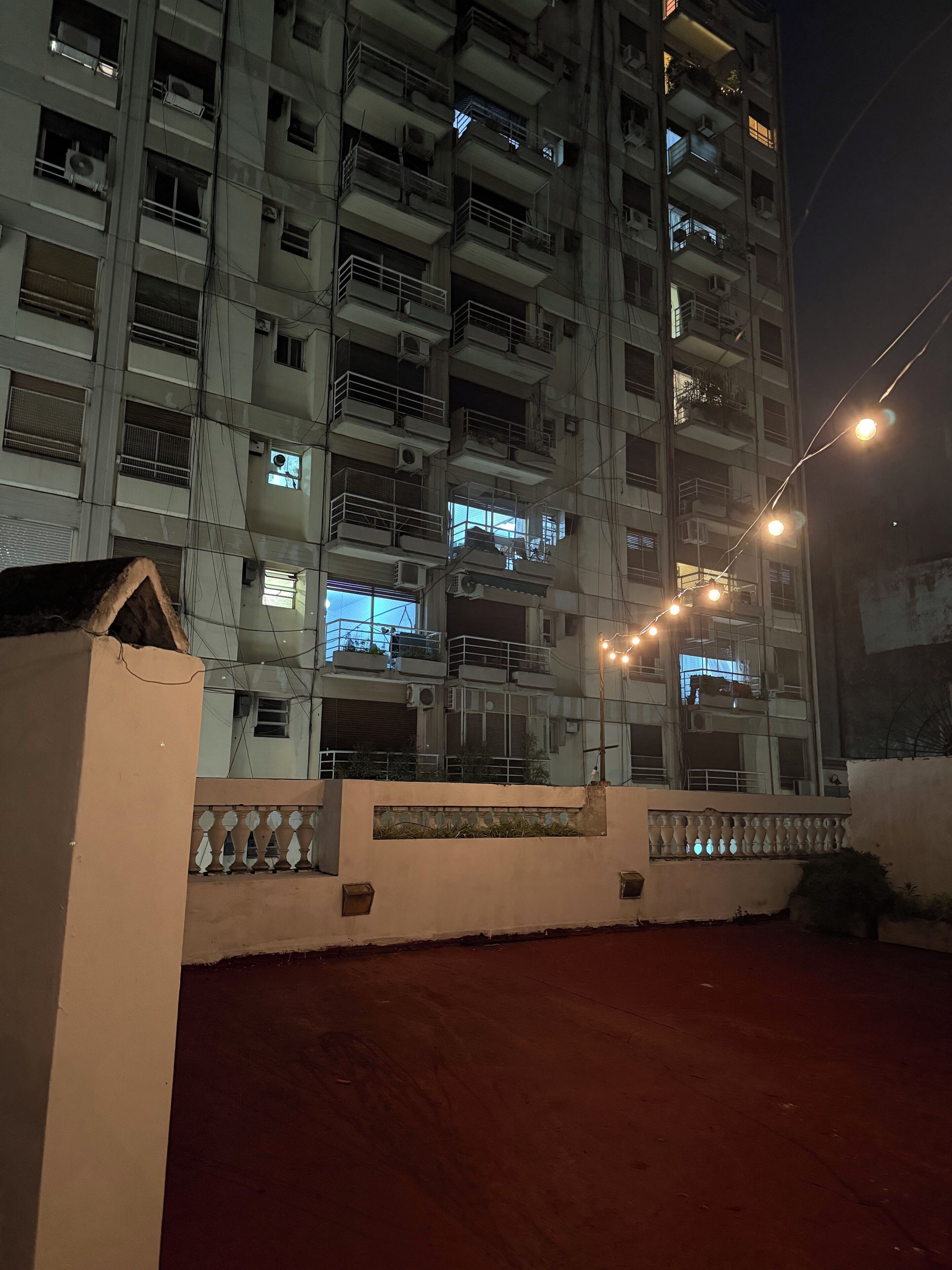 Un edificio de varios pisos con balcones, unidades de aire acondicionado y una entrada protegida por una puerta.