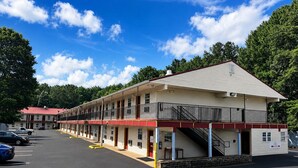 Un motel con varias habitaciones, una zona de estacionamiento techada y una escalera que lleva a la entrada.