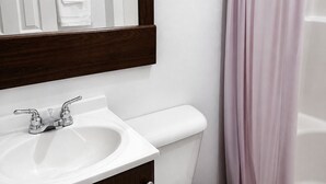 Un baño con lavamanos blanco, inodoro, espejo y cortina de ducha rosa.