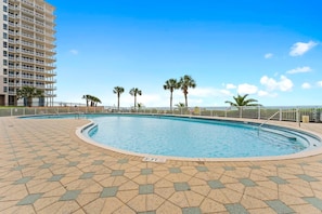 A swimming pool with a tiled deck, surrounded by palm trees and a high-rise building. - Beach Colony East 2D (Pensacola)
