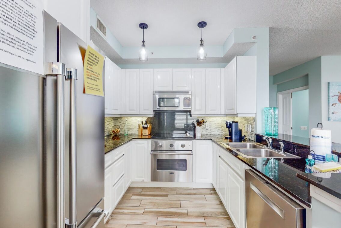 A kitchen with white cabinets, stainless steel appliances, and a herringbone floor pattern.