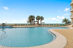 A swimming pool with palm trees, a covered seating area, and a building with balconies. - Beach Colony East 2D (Pensacola)