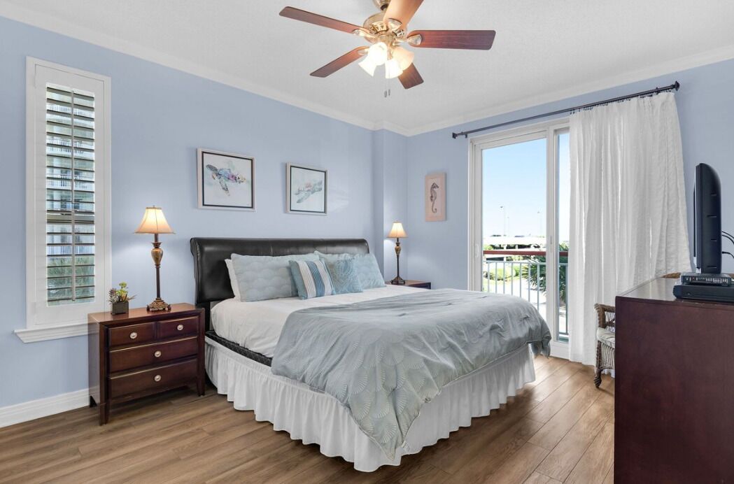 A bedroom with a bed, nightstands, a ceiling fan, a window with blinds, and a view of the outdoors.