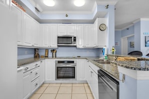 A kitchen with white cabinets, a microwave, an oven, a sink, and a clock on the wall. - Beach Colony East 2D (Pensacola)