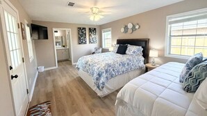 A bedroom with two beds, a ceiling fan, a TV, and a window.