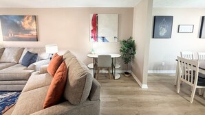 A living room with a sofa, a dining table with chairs, and a small table with a lamp.