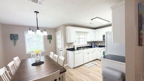 A modern kitchen with white cabinets, a wooden dining table, and a built-in oven.