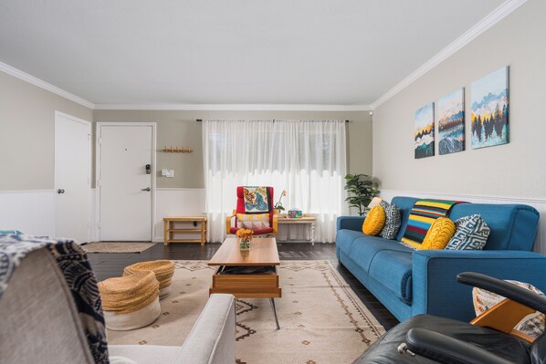 A living room with a blue sofa, a wooden coffee table, a red chair, and a white door.
