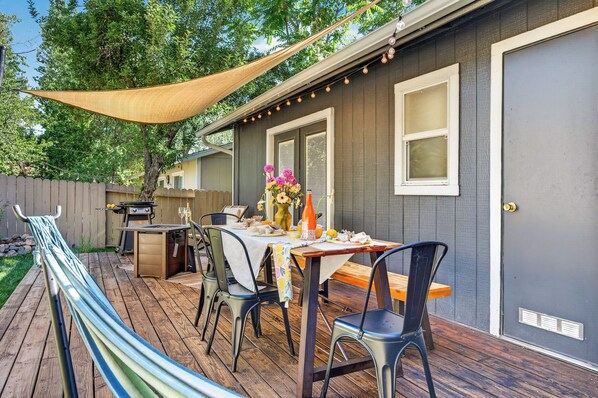 An outdoor patio with a table set for dining, surrounded by chairs, and a hammock.