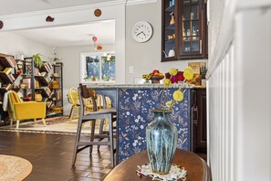 A living room with a dining area, a bookshelf, a clock, and a window with a view of the outdoors.