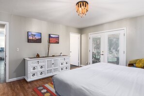 A bedroom with a bed, a dresser, two wall-mounted pictures, a ceiling light fixture, and a door with blinds.