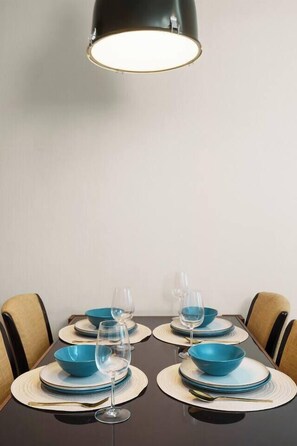 A dining table with blue bowls, wine glasses, and a black pendant light. - MonthlyStays/1GbWiFi/FullKitchen/ComfyKingBed/Tub (Watthana)