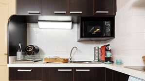 Une cuisine moderne avec des meubles de couleur bois foncé, un plan de travail blanc, un four à micro-ondes encastré, une machine à café et un évier.