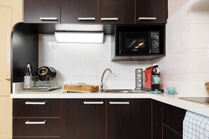 A modern kitchen with dark wood cabinets, a white countertop, a built-in microwave, a coffee machine, and a sink. - MonthlyStays/1GbWiFi/FullKitchen/ComfyKingBed/Tub (Watthana)