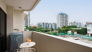 Un balcon avec une table et des chaises, donnant sur un paysage urbain avec de hauts immeubles.