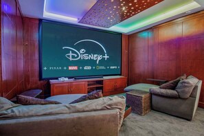 Una sala de estar acogedora con un televisor de pantalla plana grande que muestra Disney+, un mueble de madera para entretenimiento, un sofá y una mesita.