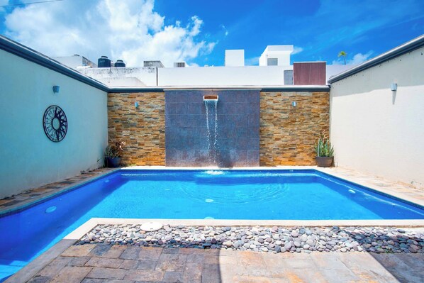 Una piscina con caída de agua, rodeada de muros de piedra y plantas en macetas.