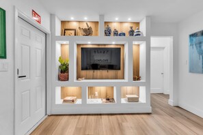A hallway with a white door, a mounted TV, and shelves with various items. - Upscale 2-bedroom "Casita" 10  min away from Bal Harbor Beach, close to mall. (Biscayne Park)