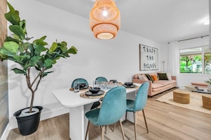 Ein zeitgemäßer Essbereich mit einem weißen Tisch, smaragdgrünen Stühlen und einem Blumentopf.