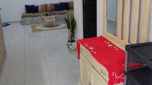 Uma sala de estar com um sofá, uma mesa de centro, um vaso de planta, um armário com um tecido vermelho e um espelho grande.