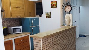 Uma cozinha com ilha central, armários de madeira, micro-ondas, relógio e ventilador.