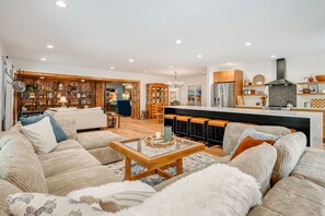 A modern living room with a sofa, a coffee table, and a kitchen area with a refrigerator and a chimney.