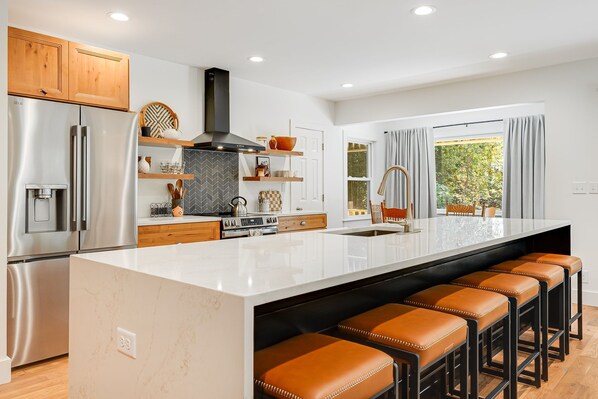 A modern kitchen with a central island, stainless steel appliances, and a large window.
